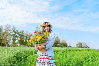 Portrait of smiling woman holding flowers while standing in farm