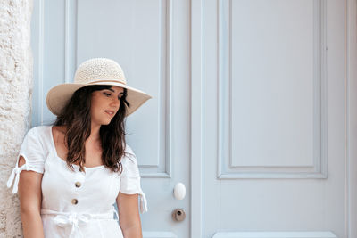 Young woman in summer outfit standing in front of pastel colored door.