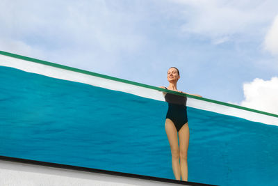 Woman standing by swimming pool against sky