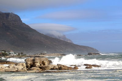 Scenic view of sea by mountain against sky