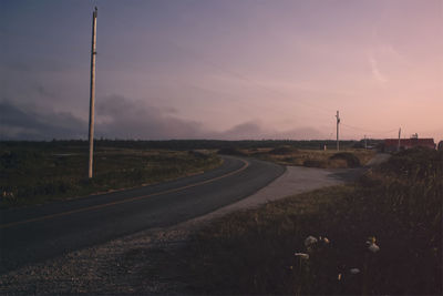 Empty road amidst field against sky during sunset