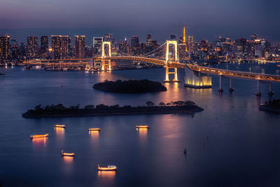 Illuminated bridge over river in city against sky at night