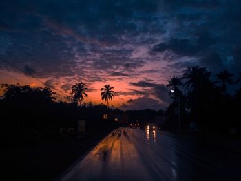 Silhouette trees by road against sky during sunset