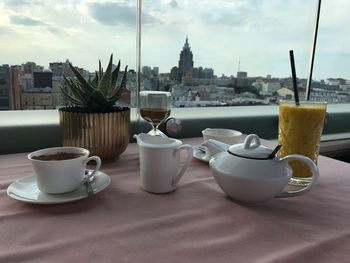 Coffee and cups on table against buildings in city