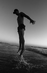 Doing exercises on the beach, jumping over the water under sunset light