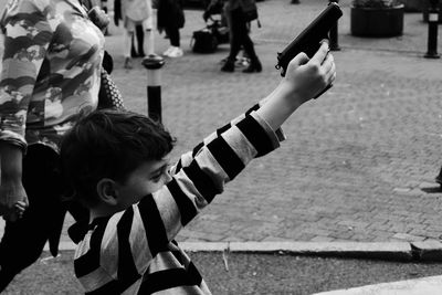 Side view of boy with arms raised holding toy gun on sidewalk