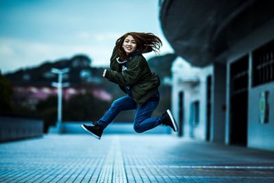 Full length of young woman jumping against building