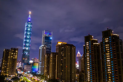 Illuminated modern buildings in city against sky at night