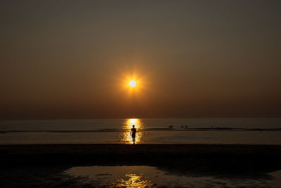 Silhouette people on beach against sky during sunset