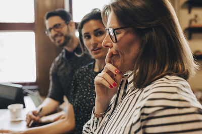 Thoughtful mature businesswoman by colleagues during discussion in office