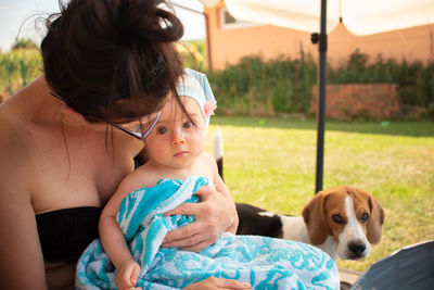 Mother holding baby girl on lap, covered with towel after swimming. summer activities.