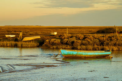 Boat moored on shore against sky during sunset