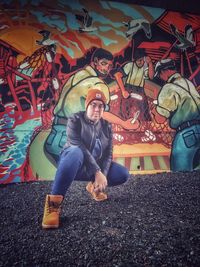 Full length portrait of young man sitting at graffiti