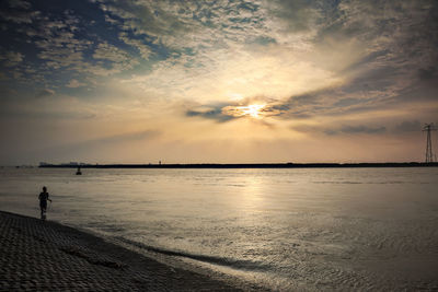 Silhouette man standing on beach against sky during sunset