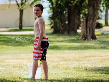 Full length of boy standing on grass against trees