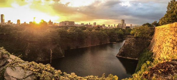 River by cityscape against sky during sunset