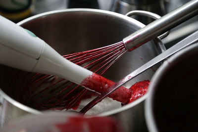 Close-up of electric mixer and wire whisk in cooking pan with red food