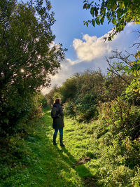 Full length rear view of woman standing amidst plants against sky