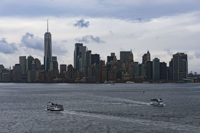 Sailboats in sea by buildings against sky in city