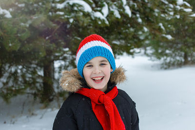 Happy boy in bright winter clothes and a red scarf walks during a snowfall