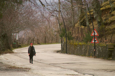 Rear view of man walking on road along trees