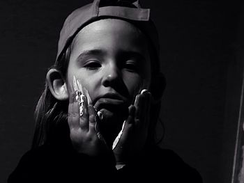 Portrait of girl applying paint on her face against black background