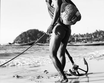 Low section of fisherman with anchor at beach against clear sky on sunny day