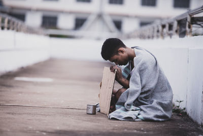 Young man sitting on sidewalk in city