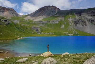 Man standing on rock by lake against sky