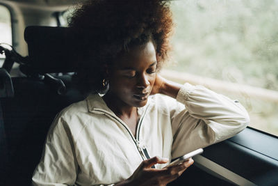 Young afro woman using smart phone while sitting in van during road trip