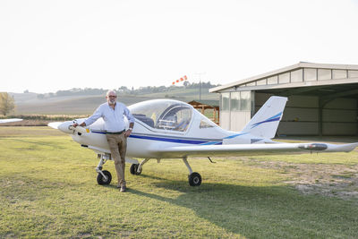 Senior man with hand on hip standing against airplane at airfield