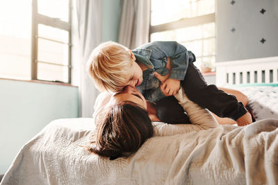 Side view of woman using mobile phone while lying on bed at home