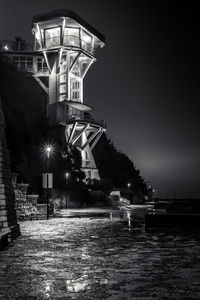 Illuminated street by building against sky at night