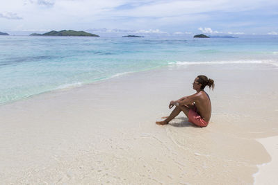 Full length of shirtless man sitting on beach