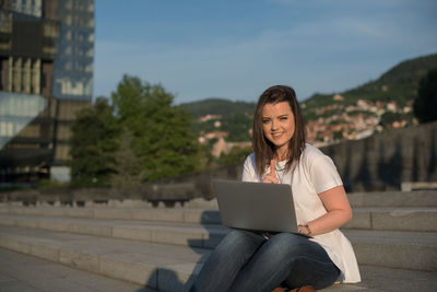 Smiling young woman using smart phone against sky
