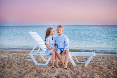 Siblings sitting on beach against sea