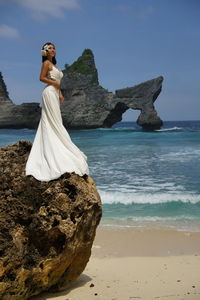 Side view of bride standing on rock by sea