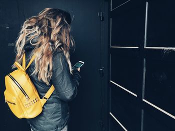 Woman with yellow backpack using mobile phone against door