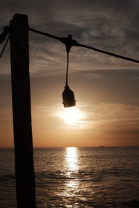 Silhouette rope hanging over sea against sky during sunset
