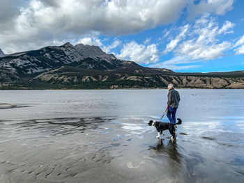 Full length of man with dog in mountains against sky in jasper, alberta