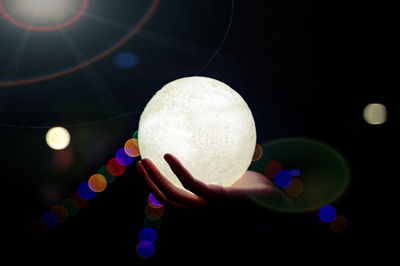 A picture of a hand holding a model of the moon at night and bokeh