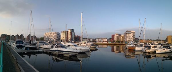 Sailboats moored in harbor against buildings in city