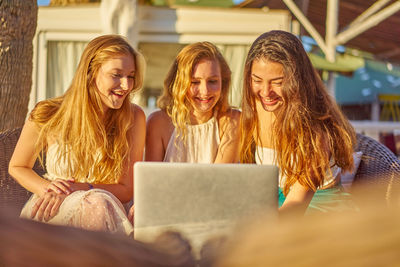 Smiling friends using laptop in city during sunny day