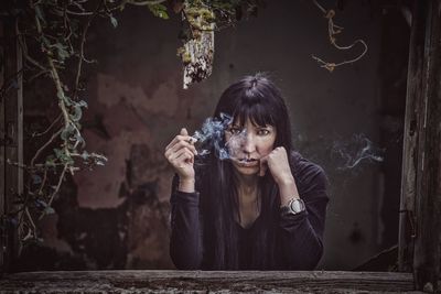 Portrait of serious woman smoking while leaning on abandoned house window