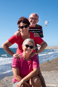 Portrait of smiling senior friends at beach against sky