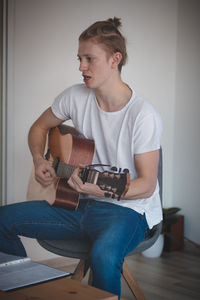 Blond man with freckles sits in the middle of a lighted room. practicing chords and songs 