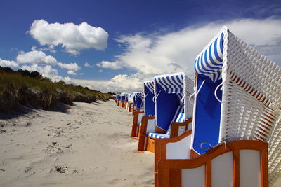 Hooded chairs on beach against sky