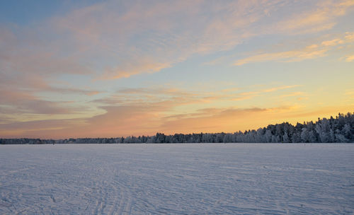 Scenic view of snow covered field against sky at sunset