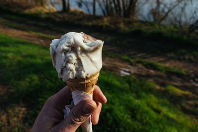 Cropped hand holding ice cream cone on field