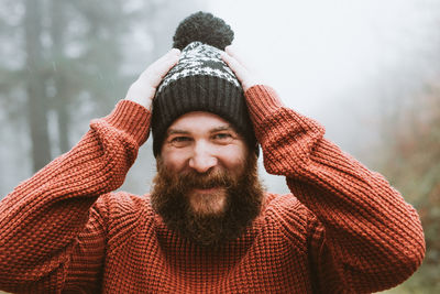 Bearded guy in sweater and hat near fir trees